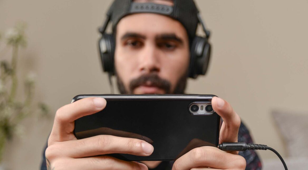 Ein Mann hat ein Headset auf seinem Kopf und spielt auf seinem Smartphone Mobile Games