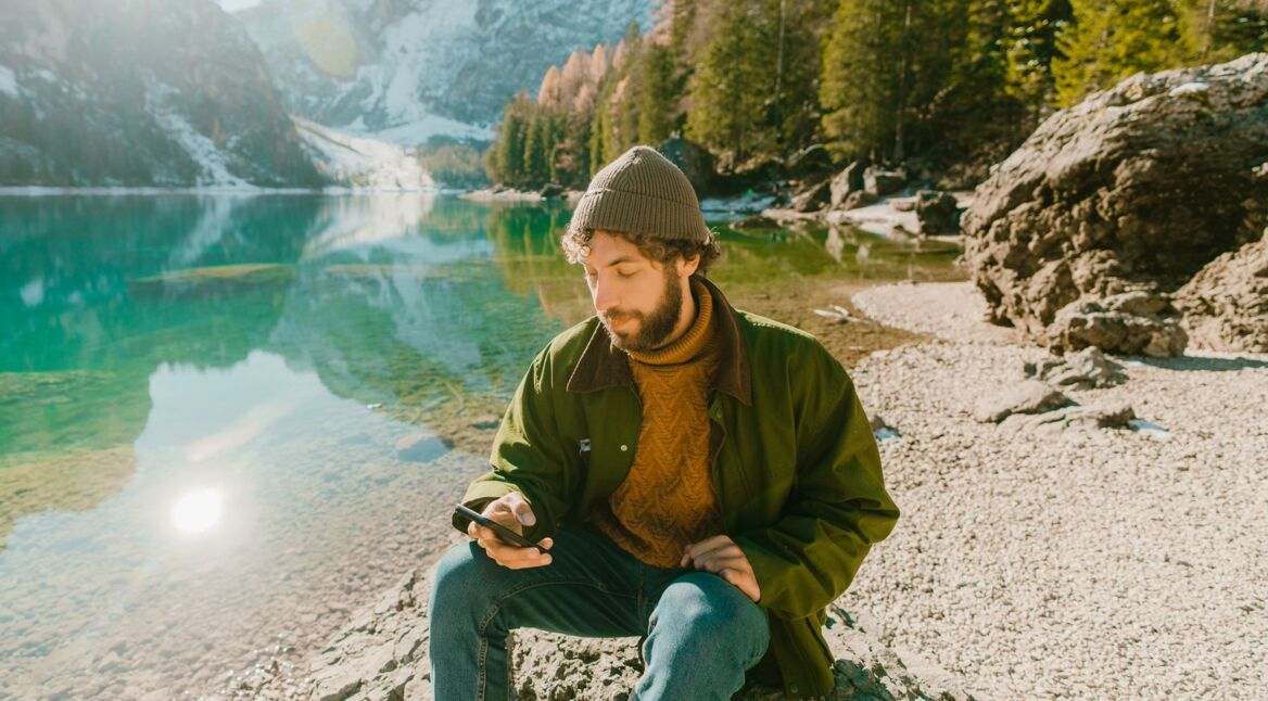 Mann sitzt am See mit seinem Galaxy-Smartphone.