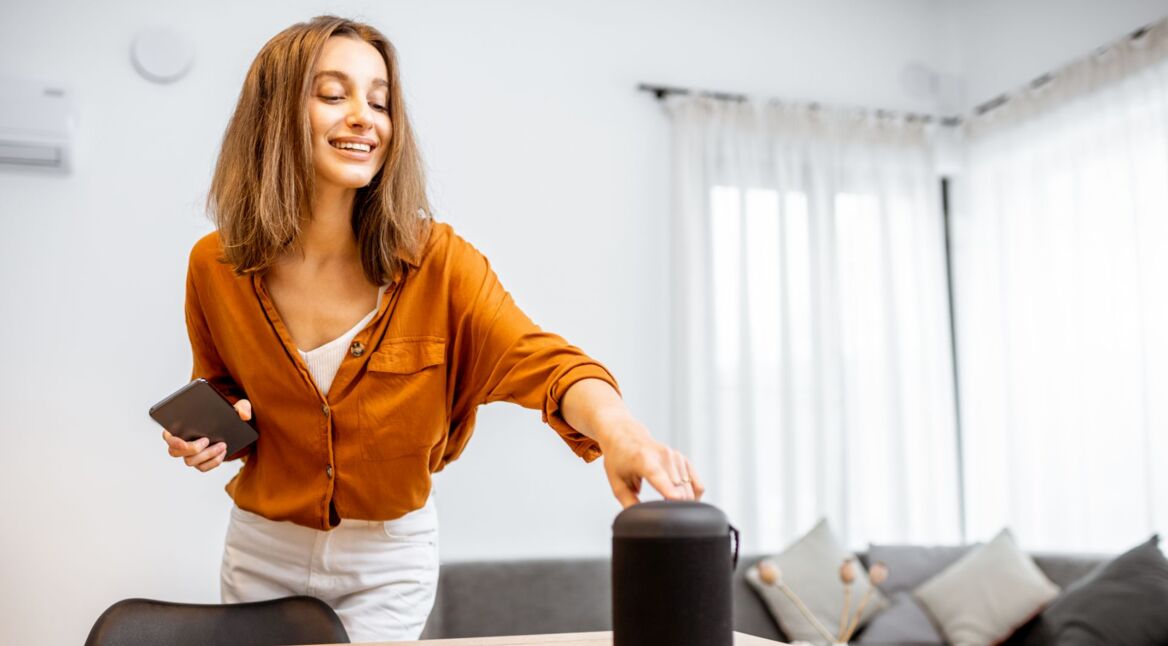 Frau mit Smartphone in der Hand tippt auf Lautsprecher von Sonos.