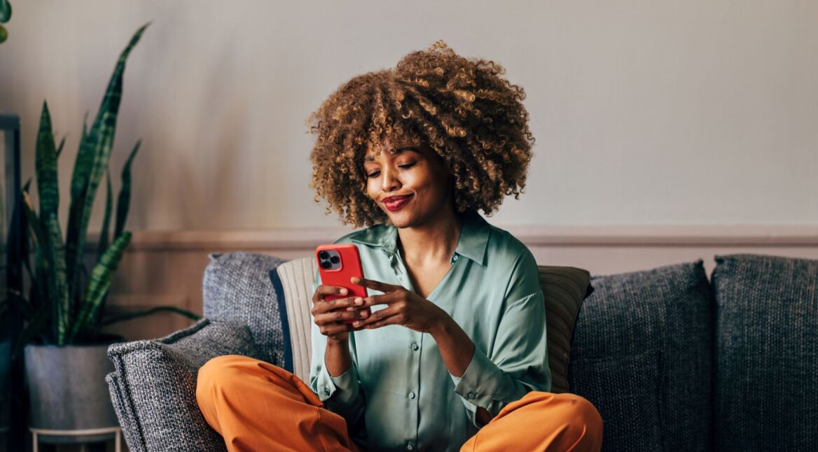 Frau sitzt auf Sofa und tippt auf iPhone.