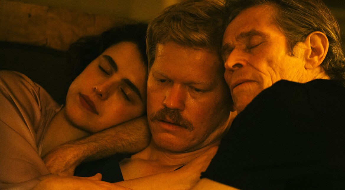 Auf dem Bild zur Kinds of Kindness Filmkritik sieht man drei Personen in inniger Umarmung. Eine junge Frau (Margaret Qualley) schläft, flankiert von zwei nachdenklichen Männern (Jessie Plemons und Willem Dafoe). Die Szene ist in warmen Farbtönen gehalten.