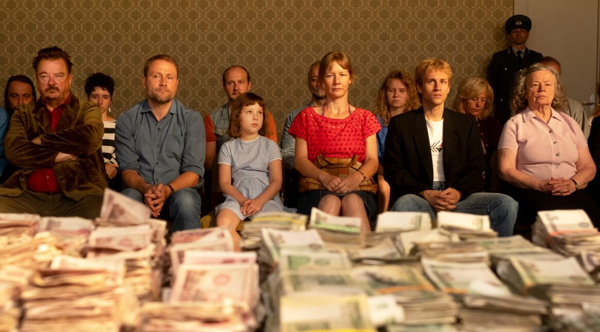 Menschen sitzen vor einem Tisch mit Geldscheinbündeln