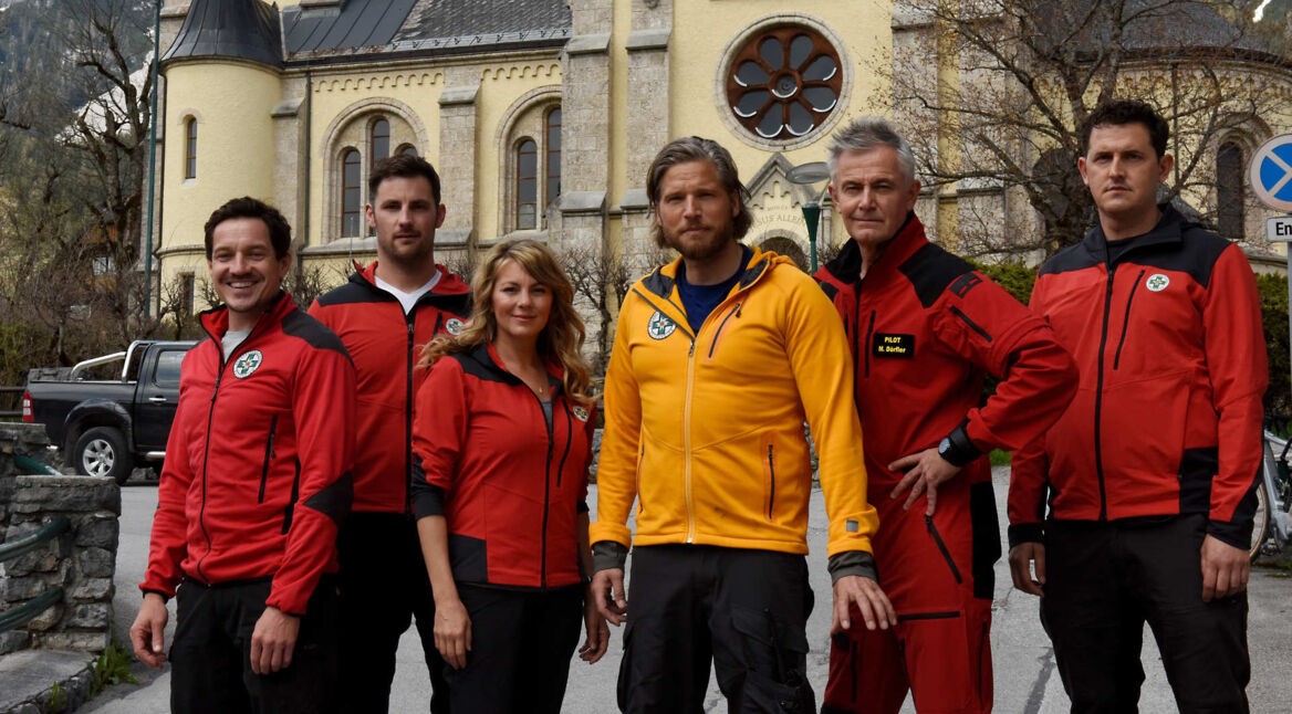 Fünf Männer und eine Frau stehen vor einer Kirche, sie tragen Uniformen des Bergrettungsdienstes