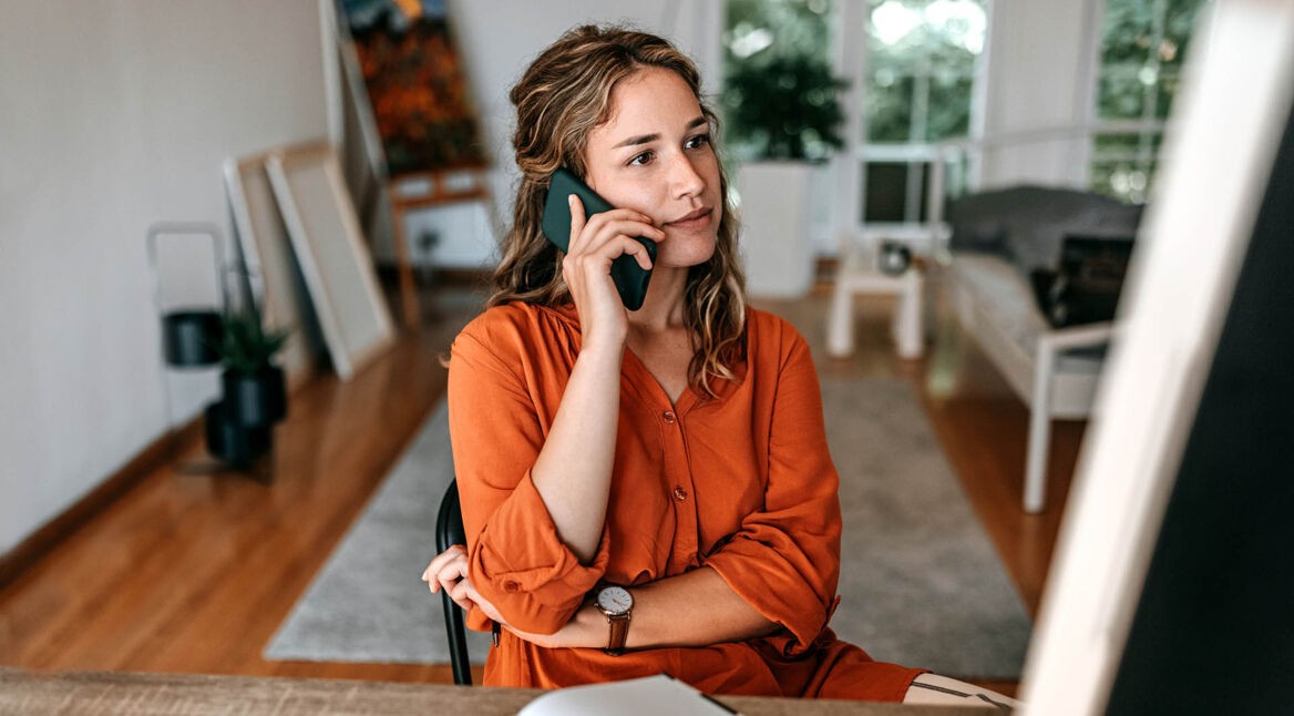 Eine junge Frau arbeitet im Homeoffice und telefoniert mit einem Smartphone