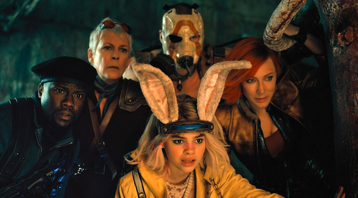 Im Bild zur Borderlands-Filmkritik sind 5 Hauptcharaktere zu sehen. Sie alle schauen erstaunt und neugierig in dieselbe RIchtung. Der Hintergrund ist dunkel, die Gesichter der Figuren werden von einer warmen Lichtquelle vor ihnen angestrahlt. Links im Bild befindet sich Roland (Kevin Hart). Erträgt eine dunkle Uniform mit schwarzer Soldaten-Kappe. Zentral im Bild und vor den anderen hockt Tiny Tina (Ariana Greenblatt). Sie hat eine gelbe Jacke an. Ihre Haare sind schulterlang und blond gefärbt. Auf ihrem Kopf trägt sie eine Art Haarreif mit plüschigen Hasenohren. Rechts im Bild ist Lilith (Cate Blanchett) zu sehen. Sie trägt dunkle Klamoten. Ihre Haare sind rot gefärbt. In der Mitte hinten steht Krieg (Florian Monteanue). Sein Körper ist von Tiny Tina verdeckt. Sein Gesicht ist ebenfalls nicht zu erkennen, denn er trägt eine weiße Maske mit einem orangenen Bogen darauf. Im Bild links von ihm ist Tannis (Jamie Lee Curtis) Gesicht zu sehen. Sie hat kurze graue Haare und trägt eine Art Sonnenbrille auf dem Kopf.