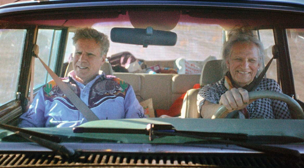 Auf dem Bild zu Will Ferrels-Netflix-Doku-Artikel fahren Will Ferrell und Harper Steele gemeinsam in einem Auto. Will Ferrell sitzt auf dem Beifahrersitz und trägt ein auffälliges Western-Hemd, während Harper Steele am Steuer lächelt. Beide wirken entspannt, die Rückbank ist mit verschiedenen Gegenständen gefüllt, was auf eine längere Fahrt oder Reise hindeutet.