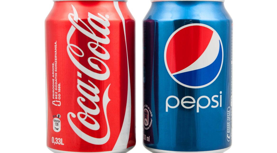 Auf diesem Bild zur "Cola Wars: Wahre Geschichte" stehen eine rote Coca-Cola-Dose und eine blaue Pepsi-Dose nebeneinander. Die Coca-Cola-Dose links trägt das ikonische weiße Logo auf rotem Hintergrund, während die Pepsi-Dose rechts das moderne Logo auf blauem Grund zeigt. Beide Dosen haben ein Volumen von 0,33 Litern und stehen symbolisch für den langjährigen Wettbewerb der beiden Marken.