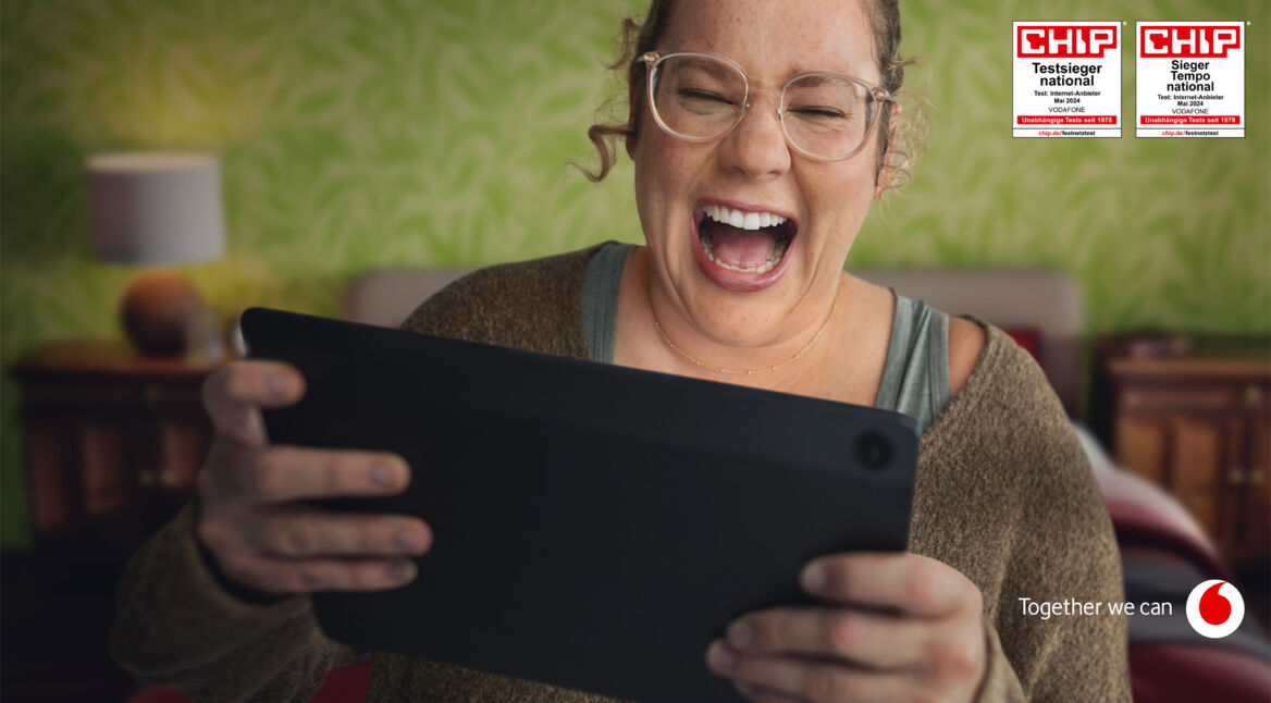 Im Bild des GoTestsieger-Artikels lacht eine Frau begeistert, während sie auf ein Tablet schaut. Im Hintergrund ist eine grüne, gemusterte Wand zu sehen. Oben rechts befinden sich zwei CHIP-Auszeichnungen, die Vodafone als führenden Internetanbieter in Deutschland kennzeichnen. Unten rechts ist der Vodafone-Slogan „Together we can“ zusammen mit dem Firmenlogo abgebildet.