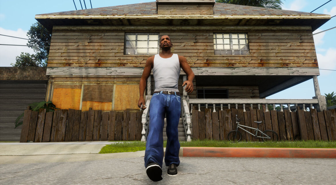 Auf dem Bild zu GTA: San Andreas Fakten ist der Hauptcharakter CJ, in weißem Tanktop und blauen Jeans, vor seinem alten, heruntergekommenen Haus in Los Santos zu sehen. Er wirkt entschlossen und schreitet selbstbewusst auf die Kamera zu. Im Hintergrund stehen ein Holzzaun und ein Fahrrad, die den vernachlässigten Zustand des Viertels widerspiegeln.