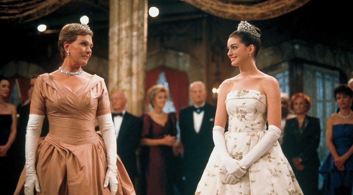 Auf dem Bild zu "Plötzlich Prinzessin 3" sind Anne Hathaway als Mia Thermopolis und Julie Andrews als Königin Clarisse Renaldi in einer eleganten Ballszene zu sehen. Beide tragen festliche Kleider: Mia ein weißes Ballkleid mit Blumenstickerei und Tiara, während Clarisse ein roséfarbenes Kleid mit langen Handschuhen und Diamantschmuck trägt. Sie tauschen ein stolzes, warmes Lächeln aus, umgeben von elegant gekleideten Gästen im Hintergrund.