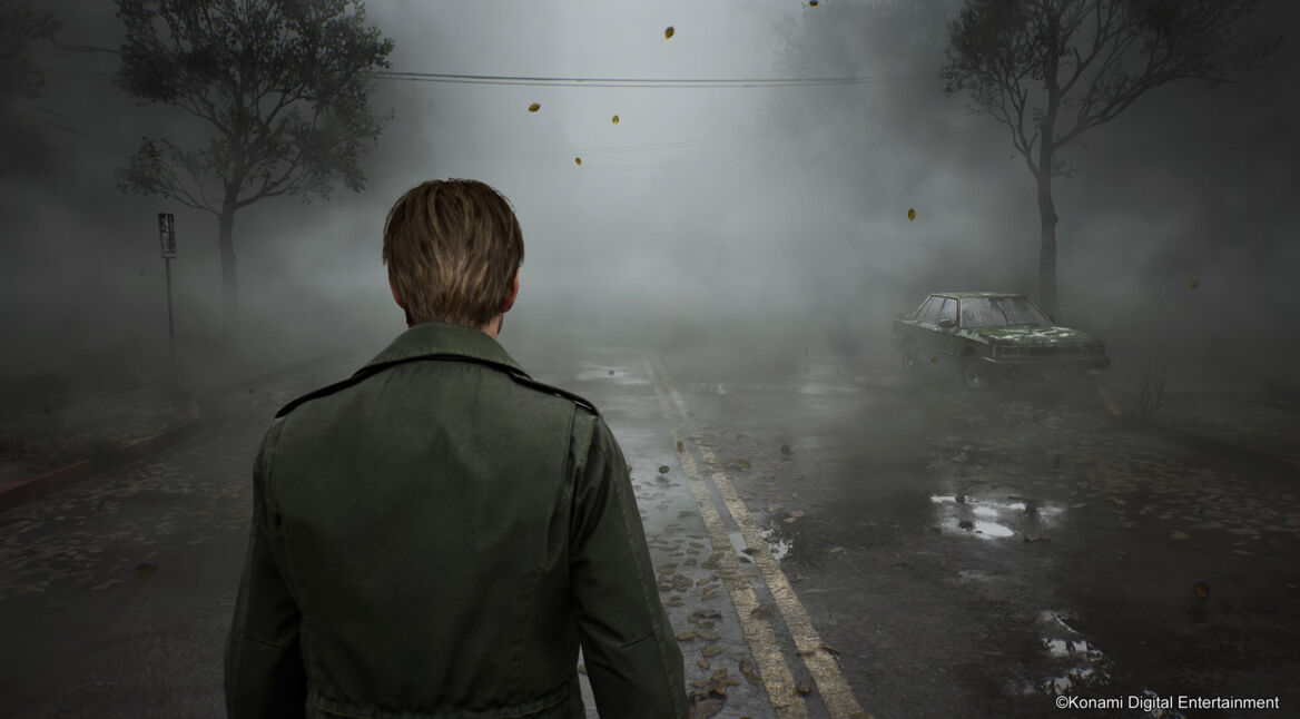 Auf diesem Bild aus dem "Silent Hill 2 Remake im Test" ist der Charakter James Sunderland von hinten zu sehen, wie er eine neblige, verlassene Straße entlangblickt. Er trägt einen langen, olivgrünen Mantel, während links und rechts kahle Bäume und ein verrostetes Auto im Nebel verschwinden. Die düstere, unheimliche Atmosphäre der Szene unterstreicht das bedrohliche und isolierte Setting des Spiels.