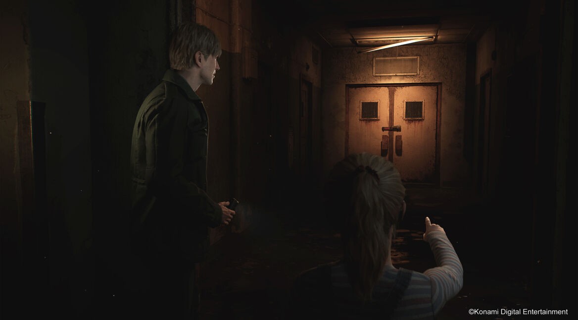 Auf dem *Artikelbild vom Silent Hill 2 Remake-Tipps-Artikel* sieht man den Protagonisten James Sunderland in einem dunklen, heruntergekommenen Korridor, begleitet von einem jungen Mädchen, das auf eine verschlossene, rostige Tür am Ende des Flurs zeigt. Die düstere Beleuchtung und der abgeblätterte Putz der Wände verstärken die unheimliche Atmosphäre des Ortes. James hält eine Taschenlampe in der Hand und blickt ernst in Richtung der Tür, während das Mädchen eine mögliche Gefahr andeutet.