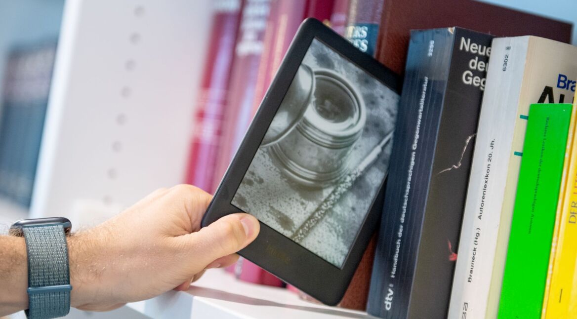 Ein Mann entnimmt ein E-Book-Reader Amazon Kindle in Berlin aus einem Buecherregal