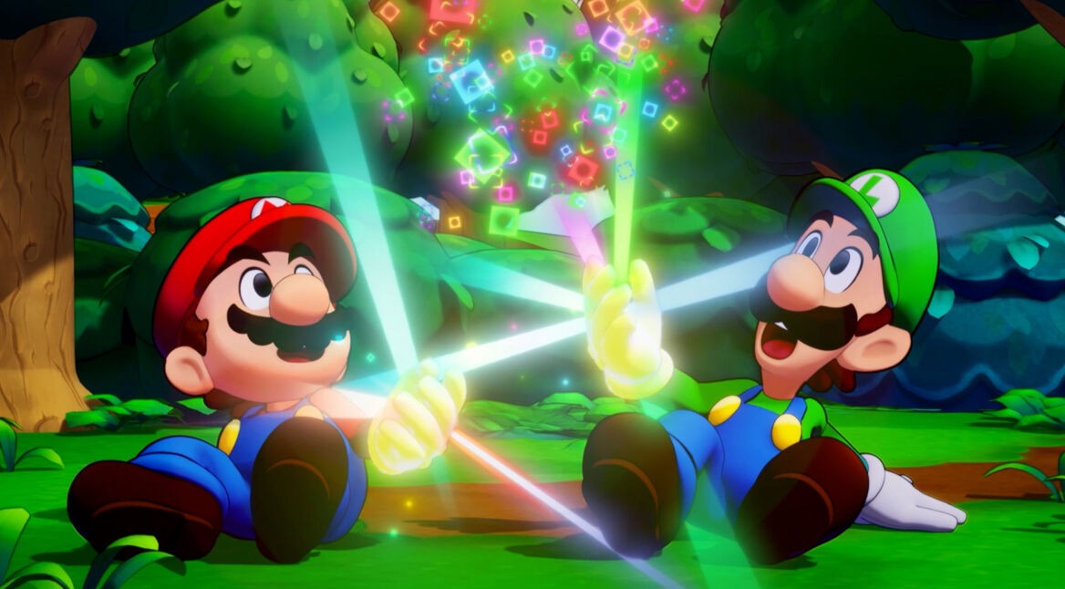 Auf dem Bild aus Mario & Luigi: Brothership Test sitzen die Brüder Mario und Luigi im Wald auf dem Boden und halten leuchtende, bunte Lichtstrahlen, die in der Luft schimmernde Quadrate erzeugen. Mario trägt seine typische rote Mütze und blaue Latzhose, während Luigi in grüner Mütze und blauer Latzhose strahlt. Beide wirken fröhlich und staunen über die magischen Effekte.