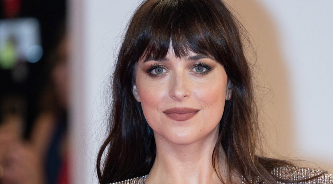 Auf dem Bild zu "Materialists" ist Dakota Johnson zu sehen. Sie trägt ein elegantes Make-up mit betonten Augen und Lippen und hat ihr braunes Haar offen, mit einem geraden Pony. Ihr Gesichtsausdruck ist ruhig und selbstbewusst. Der Hintergrund ist unscharf, was den Fokus vollständig auf sie lenkt.