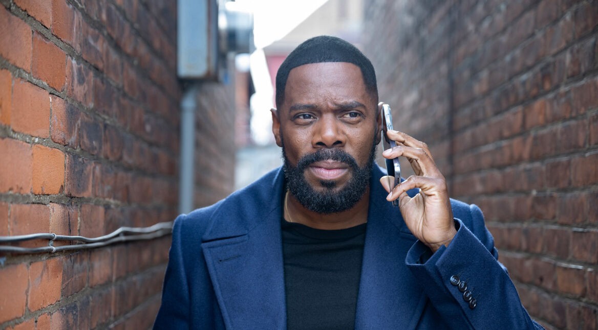 Auf dem Bild zur Serie The Madness ist Colman Domingo als Muncie Daniels zu sehen. Er steht in einer schmalen Gasse zwischen Backsteinmauern, trägt einen dunkelblauen Mantel und hält ein Smartphone ans Ohr. Sein Gesichtsausdruck wirkt nachdenklich und konzentriert, passend zu einer ernsten Szene der Serie.
