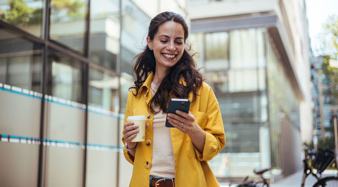 Eine Frau hält einen Kaffee und ein Handy in der Hand