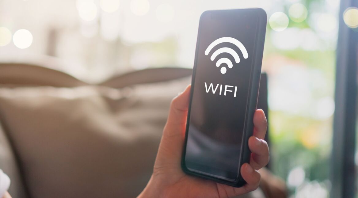 Das Wort "Wi-Fi" und das Symbol für WLAN sind auf einem Handy abgebildet, das jemand hochhält.