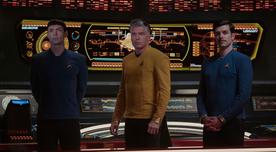 Auf dem Bild in den GigaTV-Highlights im Januar 2025 ist eine Szene aus der Serie Star Trek: Strange New Worlds zu sehen. Im Zentrum steht Captain Christopher Pike, gespielt von Anson Mount, in einer gelben Uniform, flankiert von Spock (Ethan Peck) und George Samuel Kirk (Dan Jeannotte), beide in blauen Uniformen.