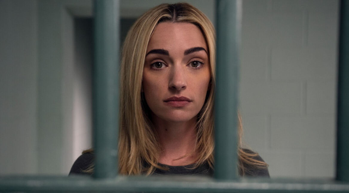 Georgia schaut in einer Gefängniszelle durch Gitterstäbe.