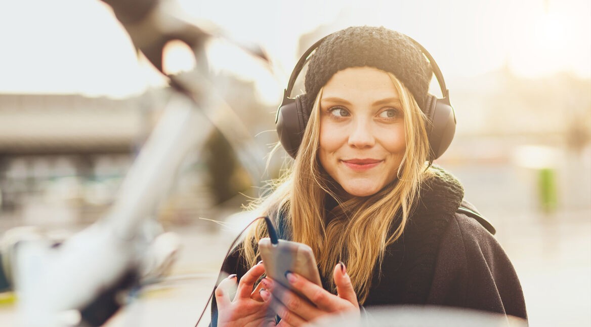 Eine junge Frau hört mit Kopfhörern Musik vom Smartphone.