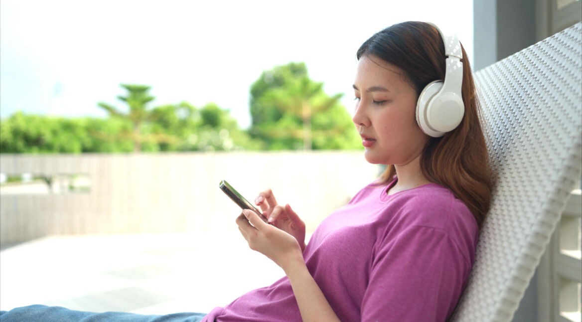 Frau im lila Shirt mit Kopfhörern schaut auf ihr Smartphone