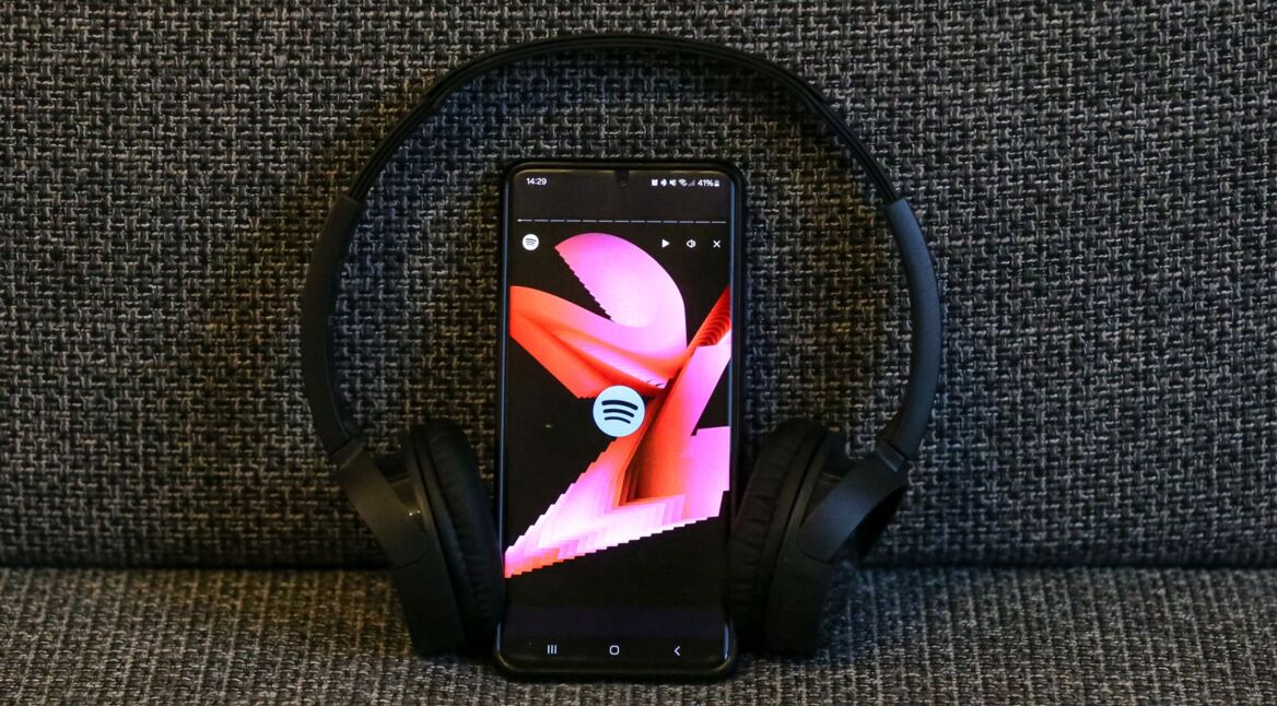 Ein Smartphone mit dem Spotify Logo und der Animation von Spotify Wrapped sowie ein Kopfhörer sind zu sehen.
