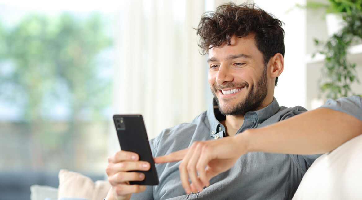 Ein Mann sitzt auf einer Couch und benutzt ein Smartphone.