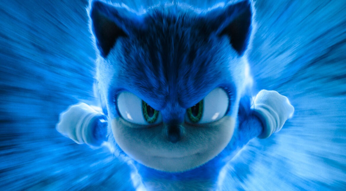 Auf dem Bild aus dem Film Sonic the Hedgehog 3 ist Sonic, die ikonische blaue Figur, in einer dynamischen Nahaufnahme zu sehen. Sein entschlossener Blick richtet sich direkt auf den Betrachter, während er mit scheinbar hoher Geschwindigkeit durch eine blaue Energiewelle rast. Das Bild ist in dem Artikel über Sonic 4 zu sehen.