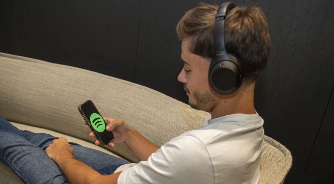 Mann mit Kopfhörern sitzt auf Couch und schaut auf sein Smartphone