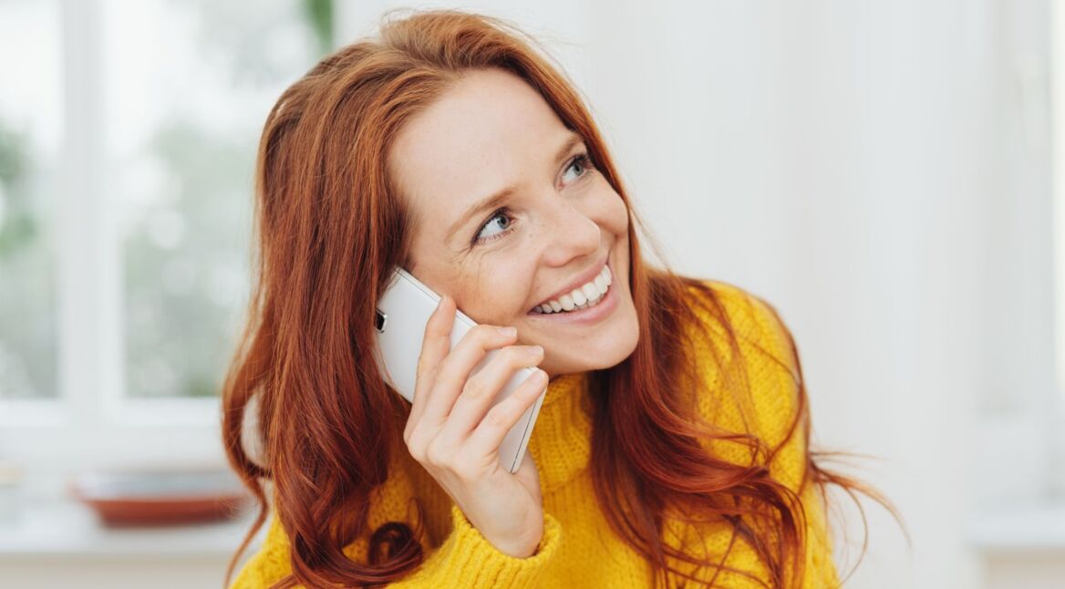 Eine lächelnde rothaarige Frau telefoniert mit dem Smartphone