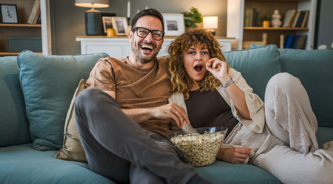 Ein Mann und eine Frau sitzen auf einem Sofa, essen Popcorn und schauen Tv