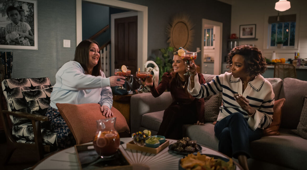 Drei Frauen stoßen in einem Wohnzimmer mit Getränken an.