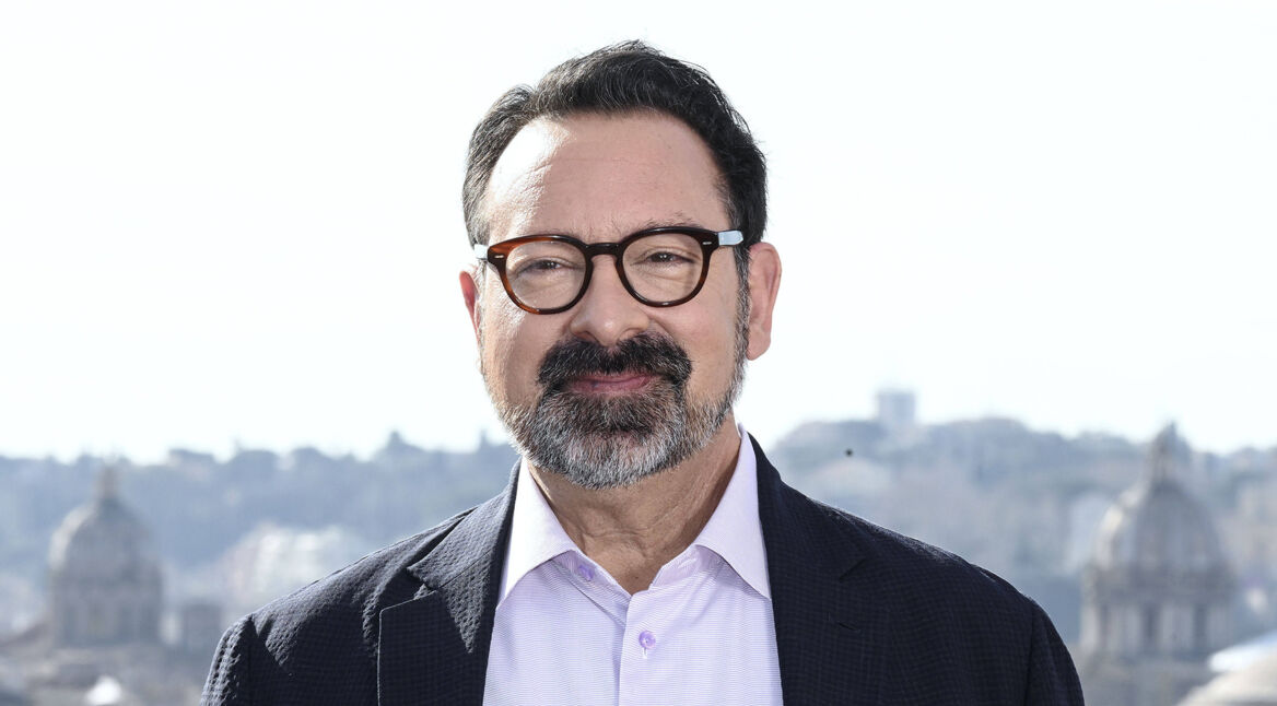 Auf dem Bild in dem Artikel zu Dawn of the Jedi ist James Mangold zu sehen. Er trägt eine dunkle Brille, hat einen gepflegten Bart und trägt ein helles Hemd mit einem dunklen Sakko. Im Hintergrund erstreckt sich eine Stadtlandschaft mit historischen Gebäuden und Kuppeln. Mangold lächelt leicht und blickt direkt in die Kamera, was eine freundliche und selbstbewusste Ausstrahlung vermittelt.