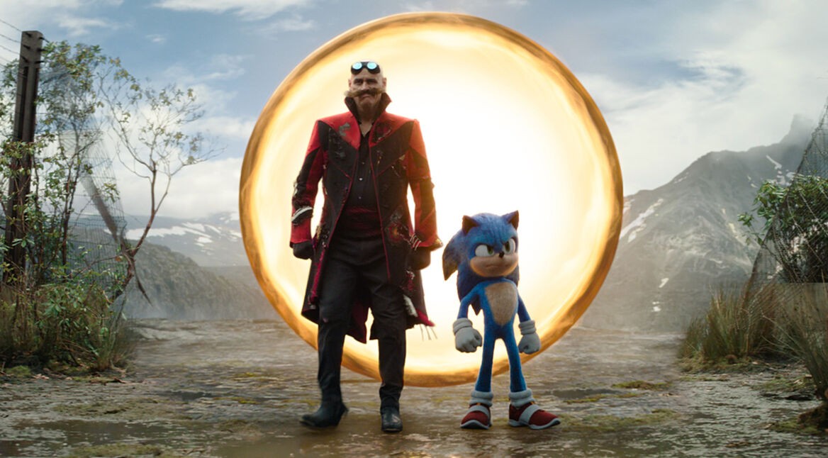 Auf dem Bild zu den GigaTV Highlights im März sind Jim Carrey als Dr. Ivo Robotnik, auch bekannt als Dr. Eggman, und Sonic zu sehen. Sie stehen vor einem leuchtenden, goldenen Portal in einer bergigen Landschaft. Dr. Robotnik trägt einen schwarzen Mantel mit roten Akzenten und eine Schutzbrille auf der Stirn, während Sonic mit verschränkten Armen entschlossen wirkt. Die Szene vermittelt Spannung und Abenteuer.