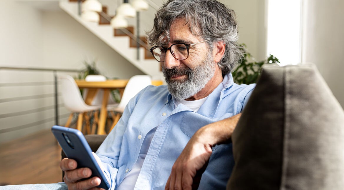 Ein Mann sitzt auf einer Couch und hält ein Smartphone in der Hand