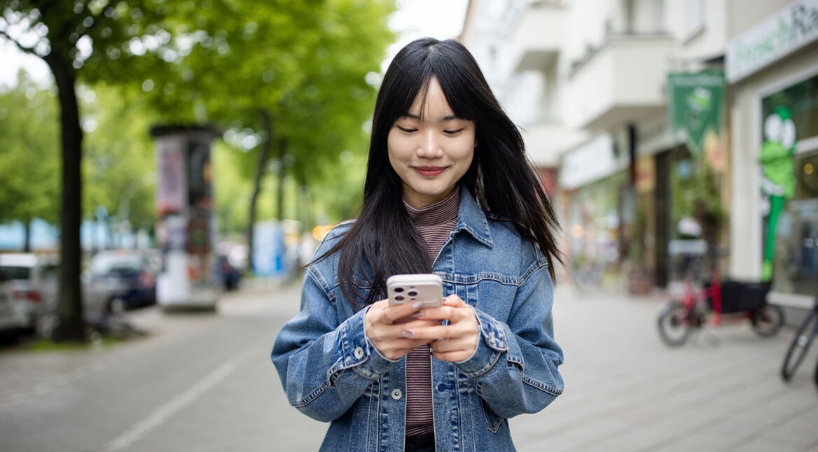 Eine junge Frau nutzt ihr Handy, während sie auf einem Bürgersteig steht