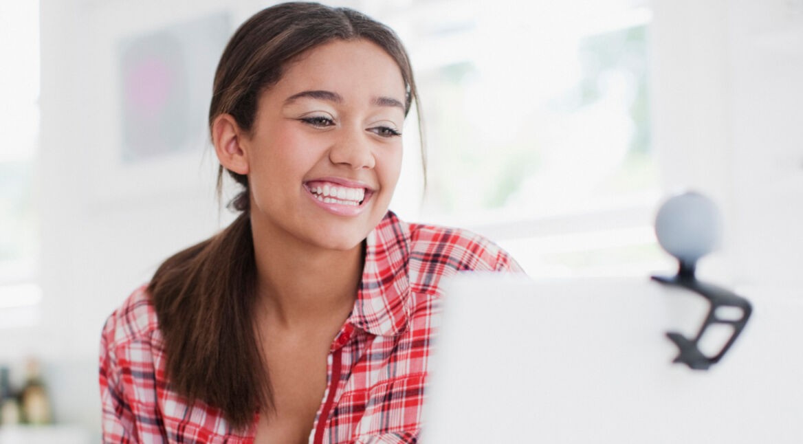 Eine junge Frau schaut in die Webcam, die an ihrem Laptop angebracht ist.