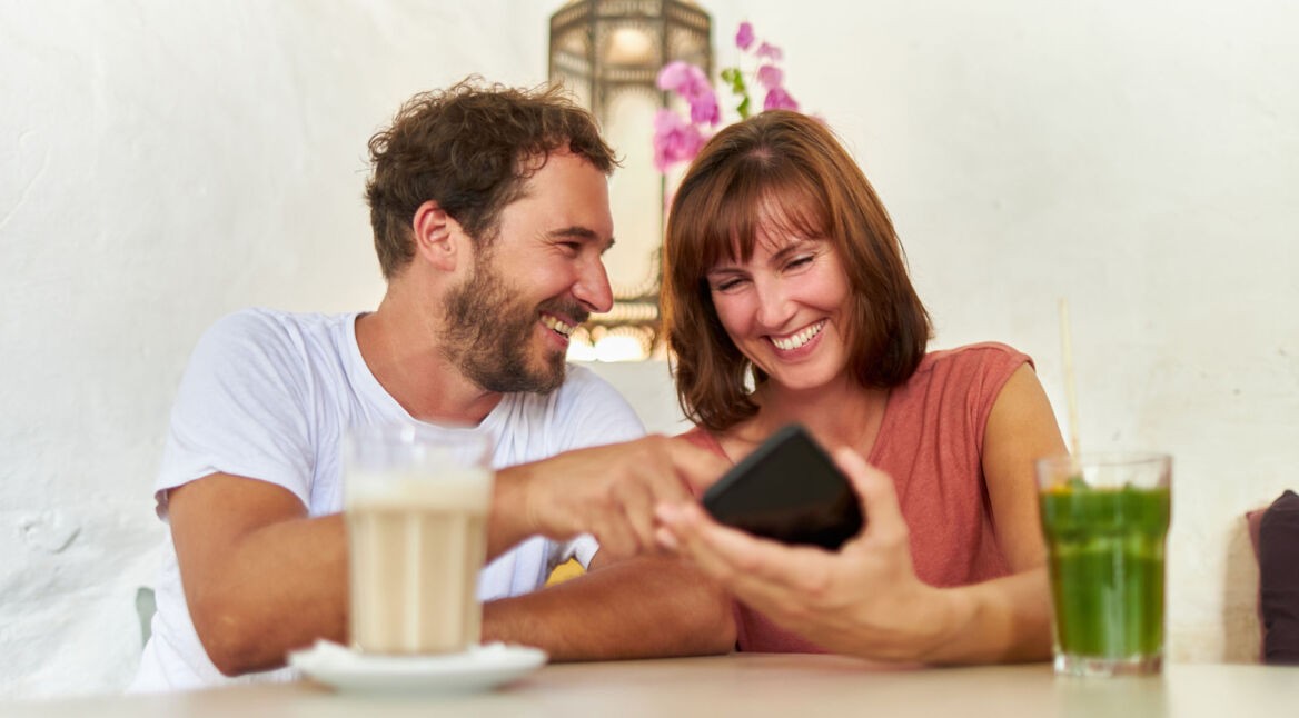 Ein Mann und eine Frau schauen auf ein Smartphone und lachen dabei.