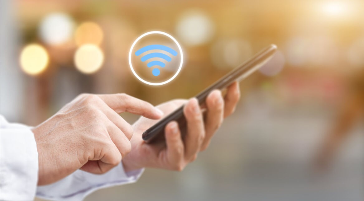 Nahaufnahme einer Hand, die ein Smartphone bedient. Darüber schwebt ein WLAN-Symol.