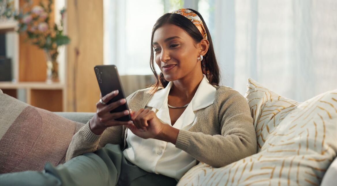 Frau sitzt auf Sofa und tippt auf ihr Android-Smartphone.