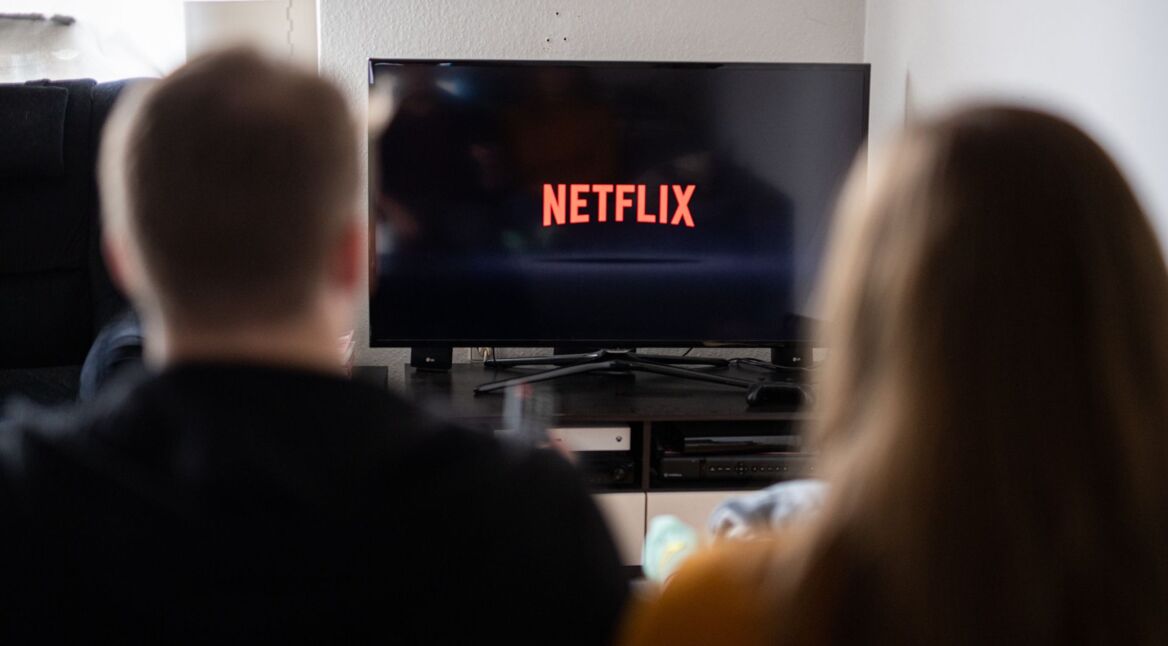 Junges Paar schaut auf einen Fernseher, auf dem das Netflix-Logo abgebildet ist
