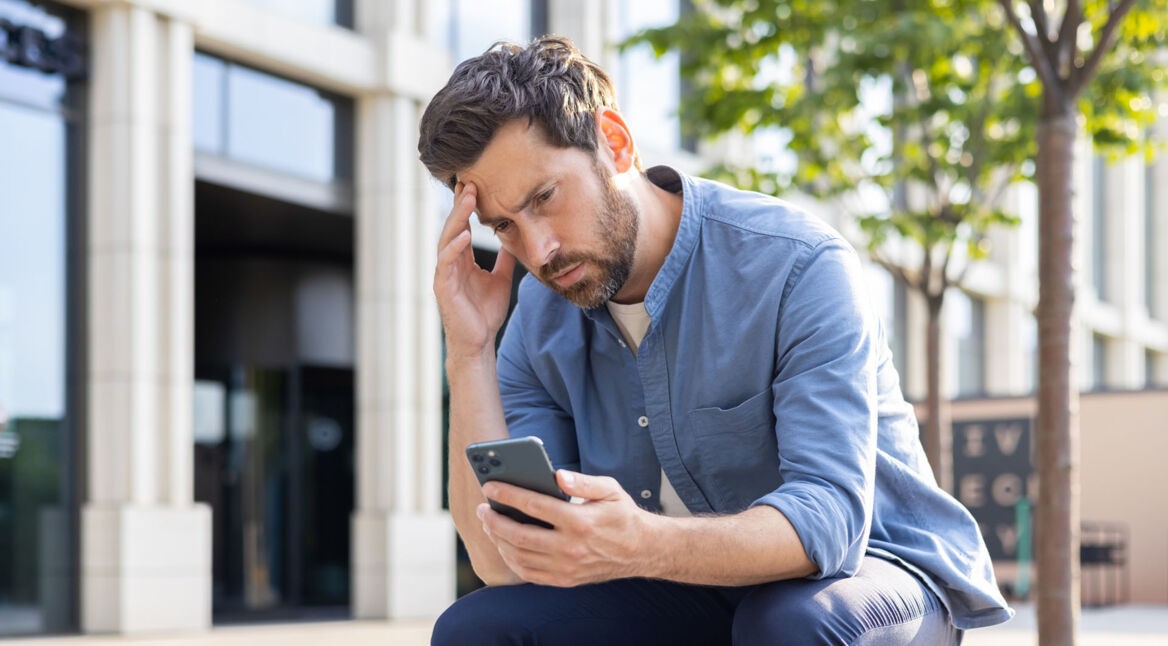 Ein Mann schaut nachdenklich auf das Display seines Smartphones.