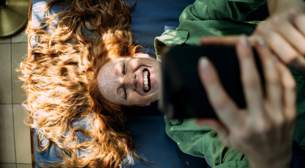 Eine junge Frau liegt auf dem Rücken und schaut auf ihr Smartphone, dass sie in beiden Händen hält.