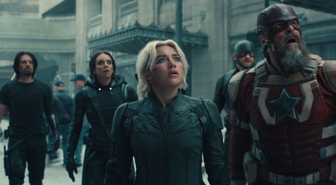 Auf diesem Bild zur Thunderbolts Kritik sind fünf zentrale Charaktere aus dem Marvel-Film Thunderbolts zu sehen. Im Vordergrund steht Yelena Belova, gespielt von Florence Pugh, mit entschlossenem Blick nach oben. Neben ihr sind Ghost (Hannah John-Kamen), Bucky Barnes (Sebastian Stan), John Walker (Wyatt Russell) und Red Guardian (David Harbour) in Einsatzmontur zu sehen. Die Szene wirkt angespannt und dramatisch, was durch die ernsten Gesichtsausdrücke und die dystopische Stadtkulisse verstärkt wird.