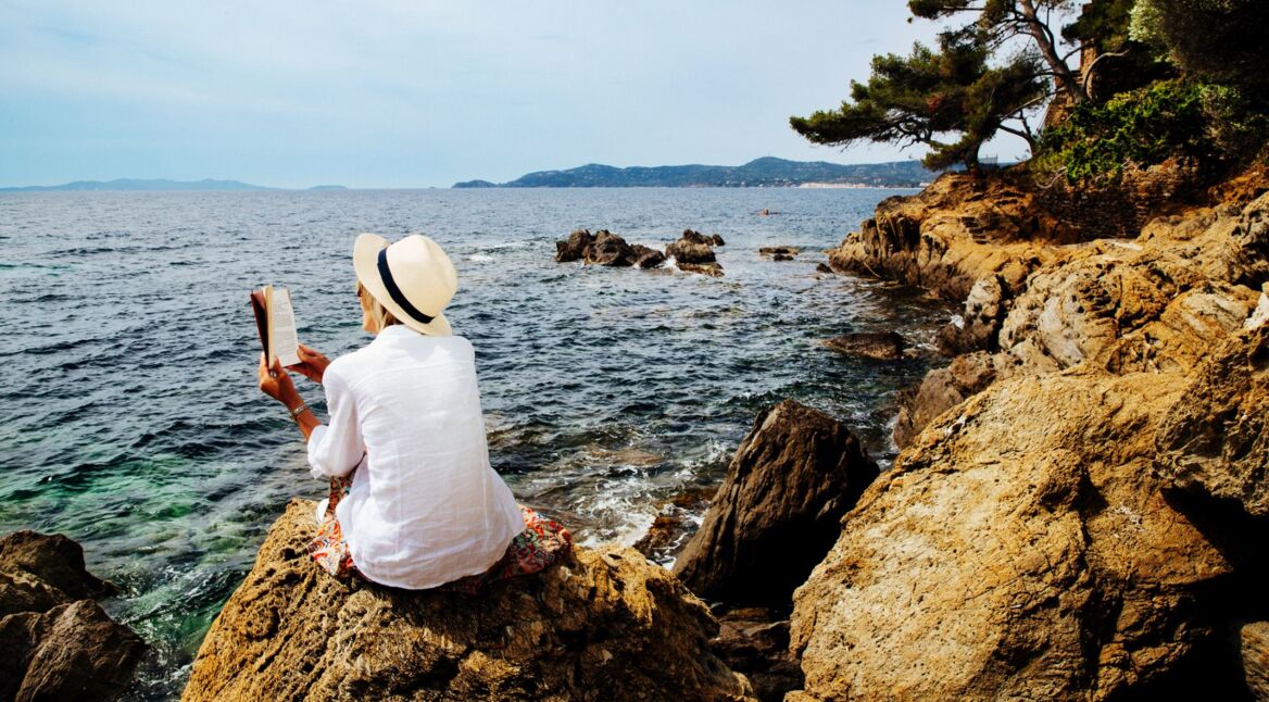 Eine Frau liest an einer felsigen Küste ein Buch