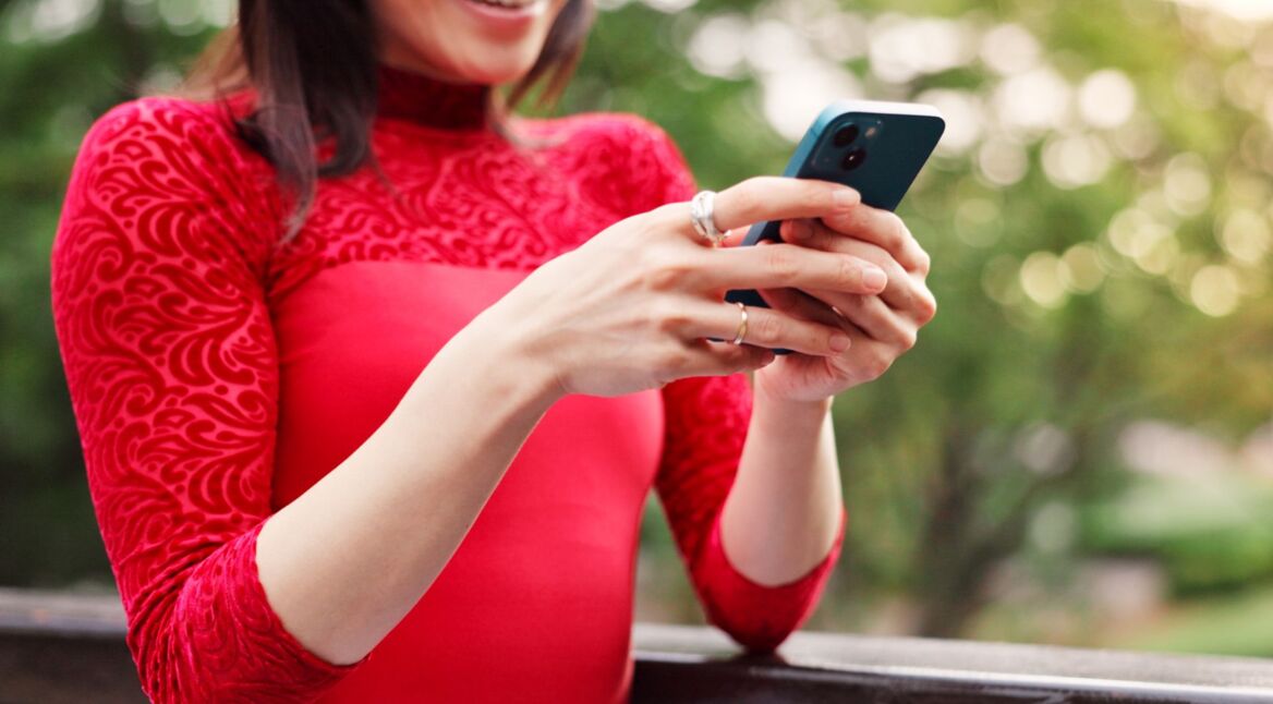 Junge Frau in rotem Shirt schaut lächelnd auf ihr iPhone.