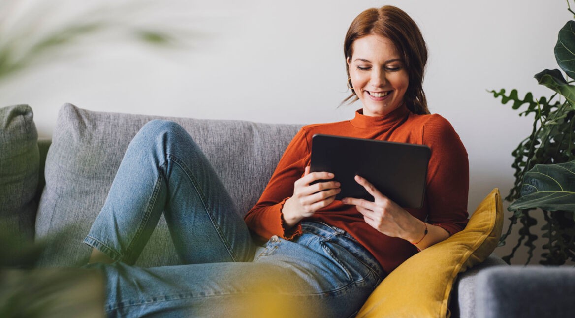 Eine Frau sitzt auf einem Sofa und benutzt ein Tablet.
