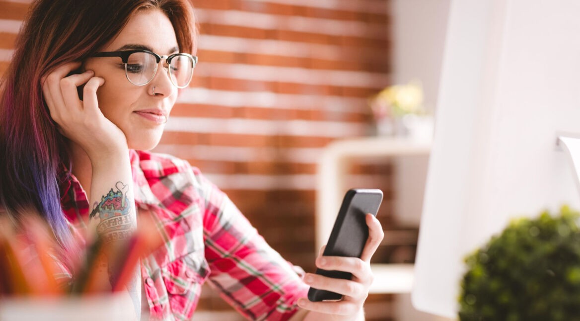 Eine rothaarige Frau schaut auf ihre Smartphone.