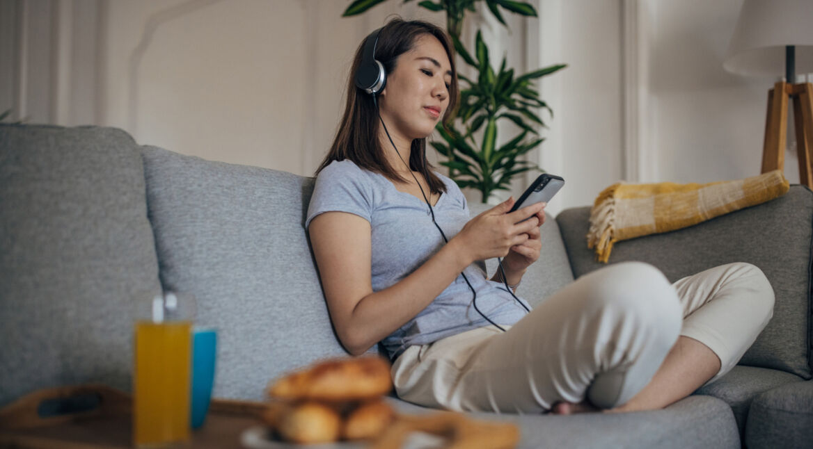 Eine Frau sitzt auf dem Sofa und hört über Kopfhörer Musik vom Android-Smartphone.